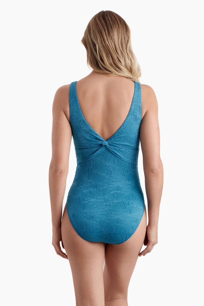 Woman faced away wearing a turqoise blue one-piece swimsuit with a textured floral print