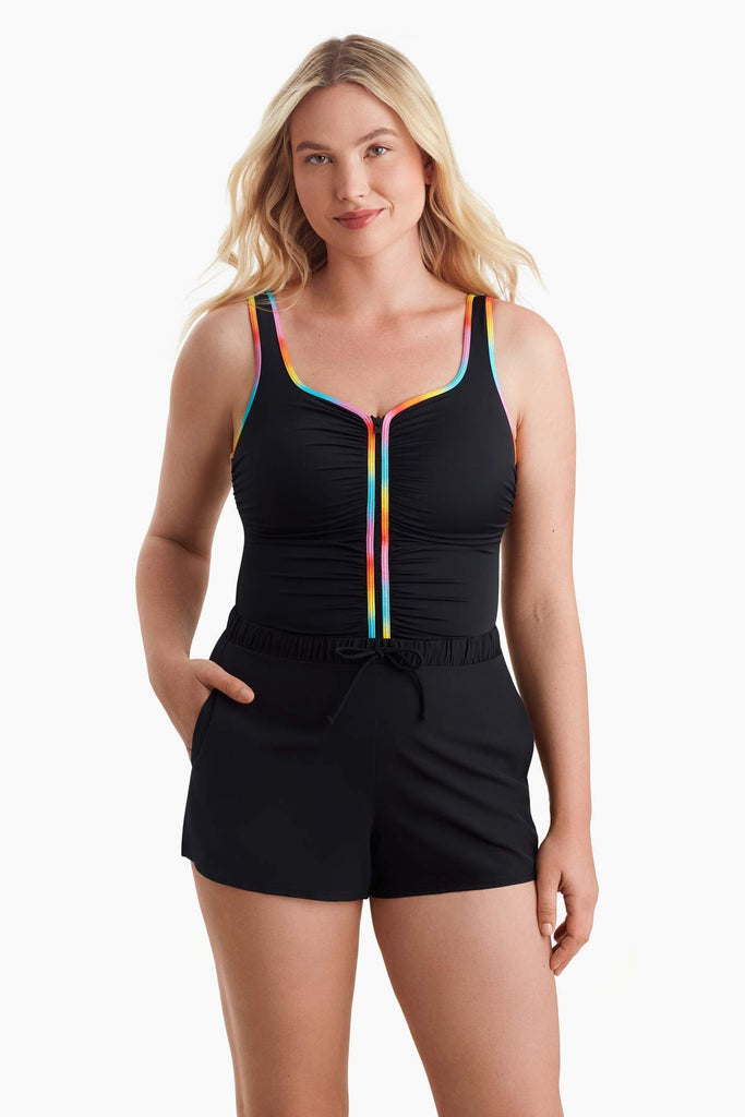 Woman wearing a one-piece swimsuit with rainbow trim on the front with her hand in the pocket